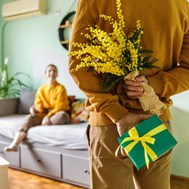 man surprising his girlfriend with a gift box and mimosa flowers