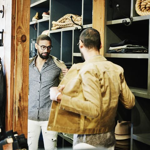 man trying on jacket while looking in the mirror in mens clothing shop