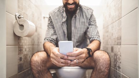 Man zit op telefoon op wc tijdens het poepen en lacht