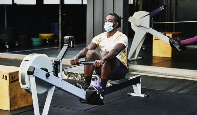 man wearing protective face mask working out on rowing machine at outdoor gym