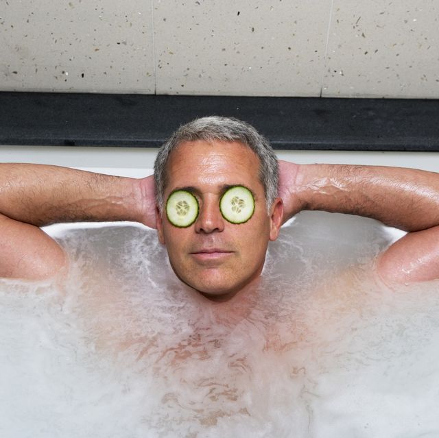 man with cucumbers atop eyes taking bath