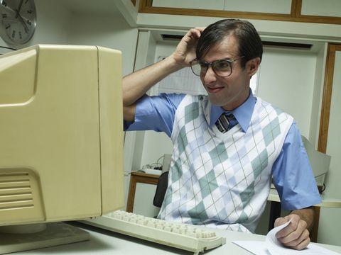 Man working at office desk, looking at computer and scratching head