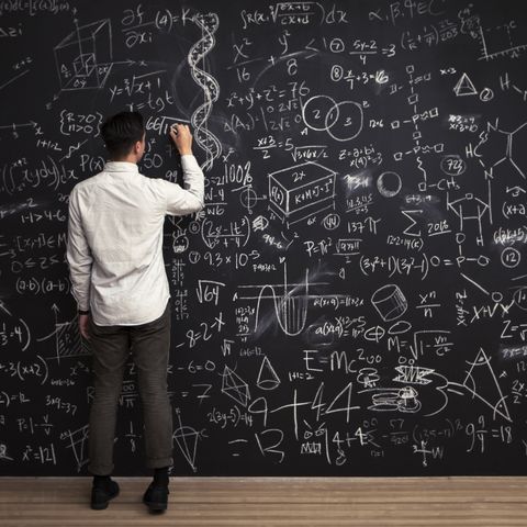 man writes mathematical equations on chalkboard
