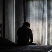 Rear View Of Man Sitting On Bed lonely young man depressed and stressed sitting in the dark bedroom, negative emotion concept