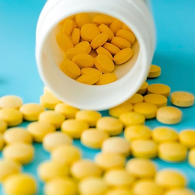 many small yellow pills spilled out of a white jar on a blue background