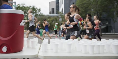 Marathon runners running, passing water station on urban street