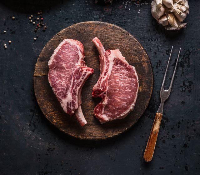 marbled raw pork chops of porco iberico meat on round cutting board with meat knife french racks