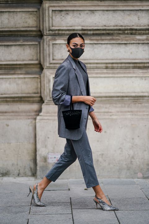 a woman walks at paris fashion week wearing a tailored gray suit and a black bucket bag