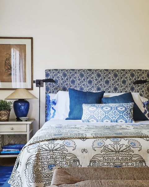 a blue and white pattern cloaks the headboard, bed skirt, and armchair cushions in a guest bedroom with a rush bench at the end