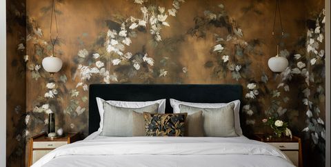 a white bed surrounded by a wallpaper that resembles a large mural and pendant lamps on either side