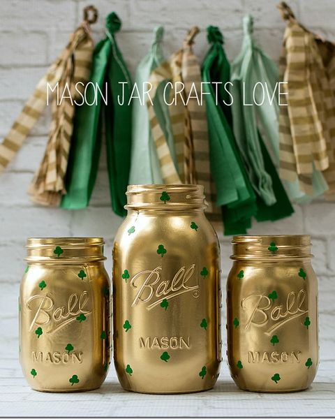 three mason jars painted gold with green shamrocks on them sitting in a row