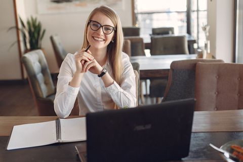 una mujer con gafas sentada en una mesa con un cuaderno y un ordenador portátil