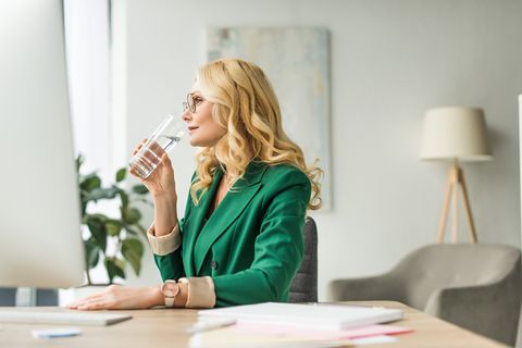mature businesswoman in eyeglasses drinking water