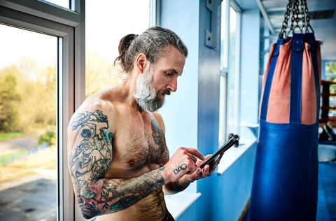 Mature man taking break from workout and using digital tablet in gym