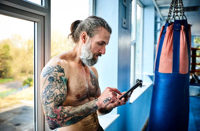 Mature man taking break from workout and using digital tablet in gym
