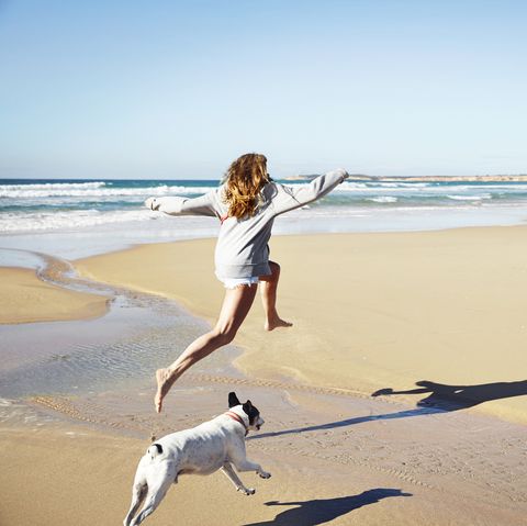 Mature woman and dog leaping over water on beach, Conil de la Frontera, Spain