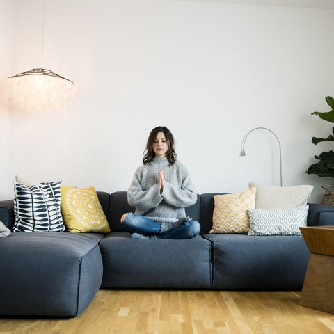 mature woman sitting crosslegged on couch with eyes closed meditating at home