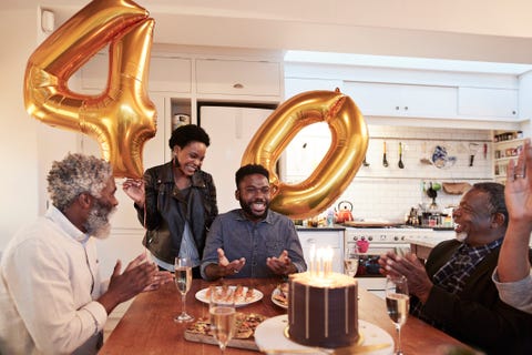 smiling woman holding number 40 helium balloons while standing by man during birthday party with family at home