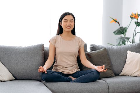 Meditation, relaxation, lazy leisure at home. Pretty, calm asian young woman in casual clothes sit in lotus position on sofa with closed eyes, smiling, meditating, unloading thoughts, calmness concept