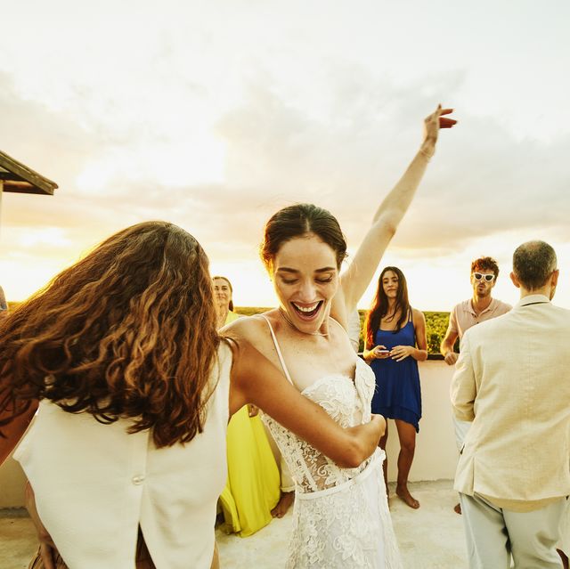 medium wide shot of smiling bride and friend dancing during party on rooftop deck after wedding at tropical resort