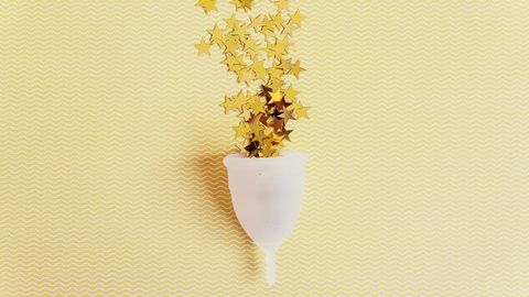 Menstrual cup with sparkling stars on yellow background