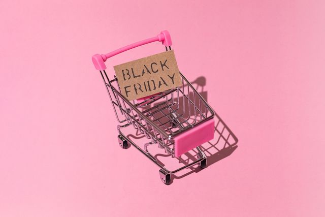 metal and pink shopping cart, with brown black friday sign with hard shadow, on pink background shopping, discounts, opportunities and black friday concept