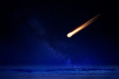 meteor in night sky falling over ocean