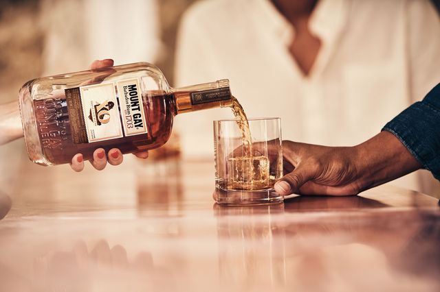 a person pouring mount gay rum xo into a glass for another person