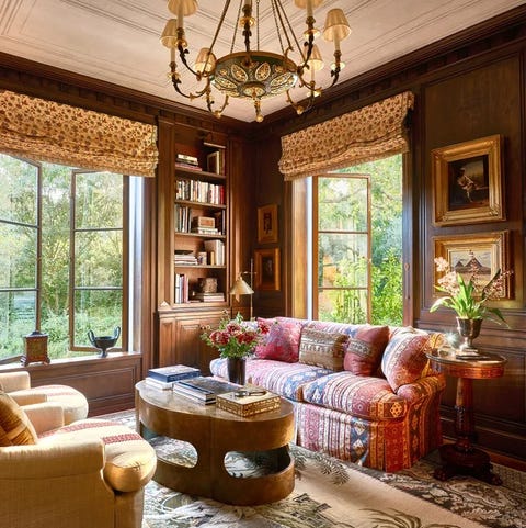 A List 2022 - ELLE DECOR living room with tall open paned windowswith colorful sofa and pillows hollowed out coffee table and elephant themed rug