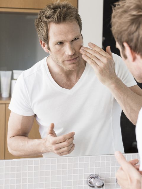 A middle-aged man looks at the bathroom mirror and puts face cream on it.