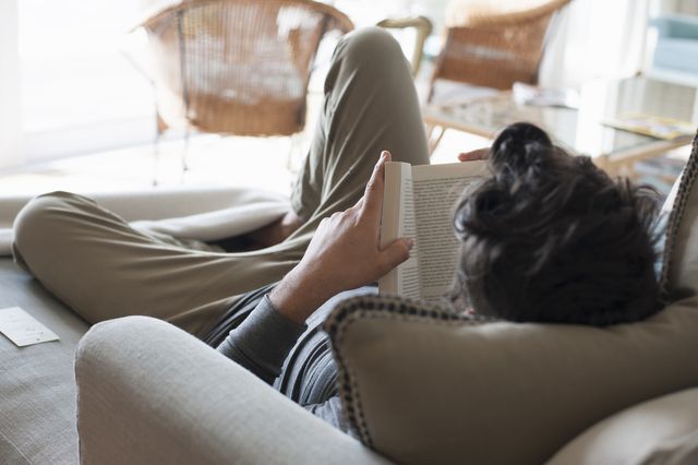 mid adult man relaxing on sofa, reading book, rear view