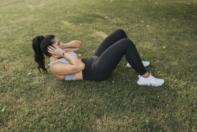 mid adult woman exercising while lying on grass at backyard