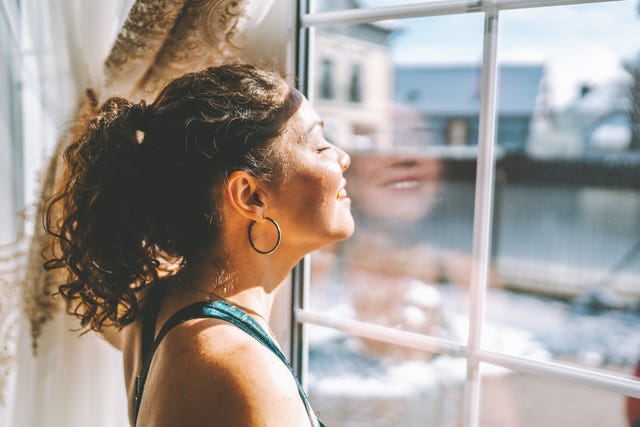 Una donna in piedi alla finestra a godersi la luce del sole