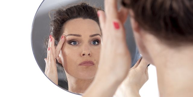 middle aged woman looks at her face in the mirror lifting sking