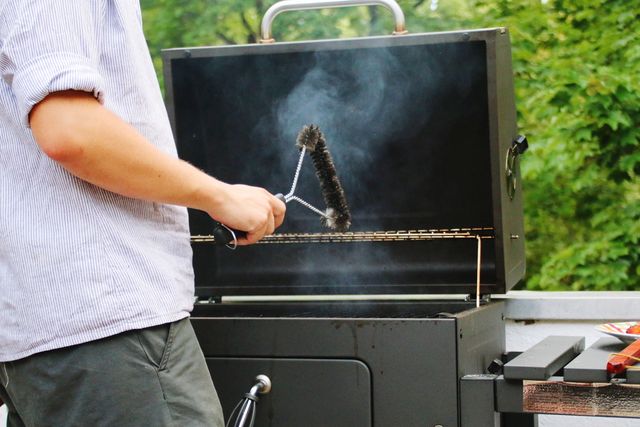 midsection of man cleaning barbecue grill with wire brush