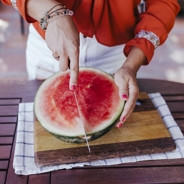 midsection of woman cutting watermelon on table