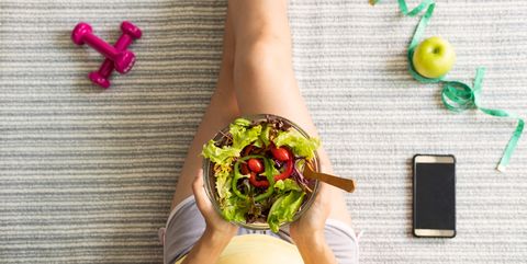midsection of woman holding salad in bowl while sitting on bed at home