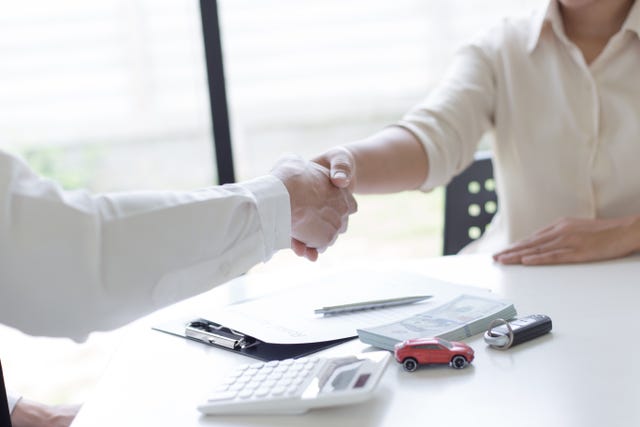 Au milieu de la femme serrant la main avec un agent d'assurance automobile au bureau