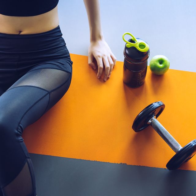 Midsection Of Woman Sitting By Water Bottle And Dumbbell