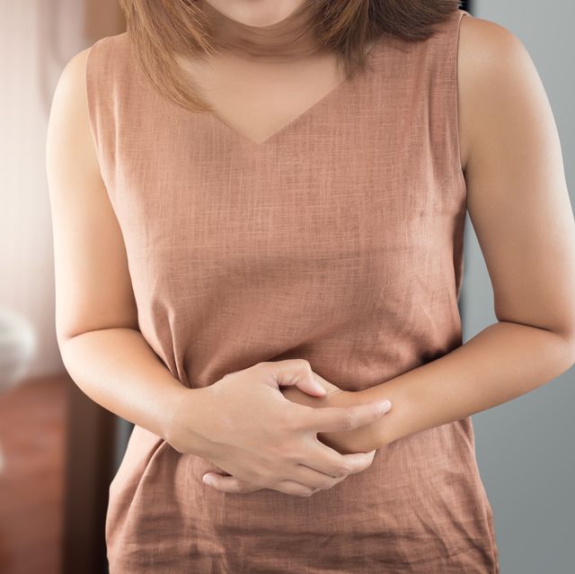 midsection of woman with stomachache standing against toilet