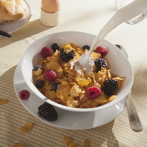 Milk being poured on a bowl of cornflakes with fruit