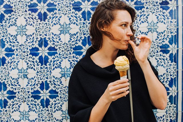 woman licking finger while eating ice cream at a tiled wall