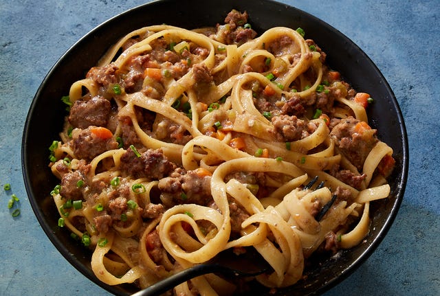 miso fettuccine bolognese garnished with chives in a black bowl on a blue background