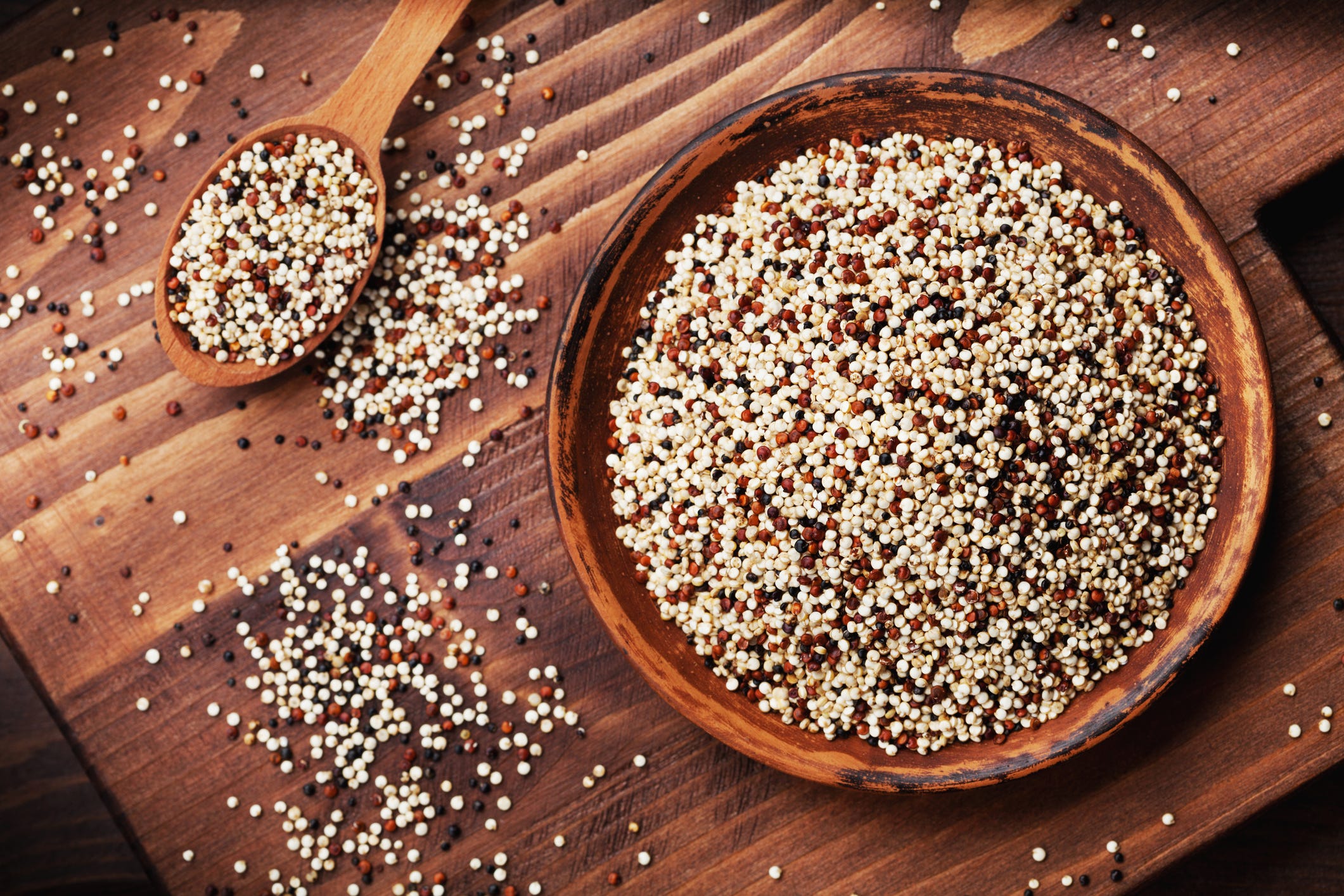  Gemischte Quinoa in Schüssel auf hölzernem Küchenbrett Draufsicht.