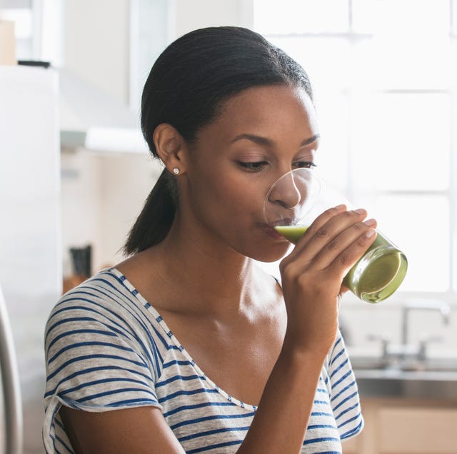 woman drinking glass of green juice in kitchen