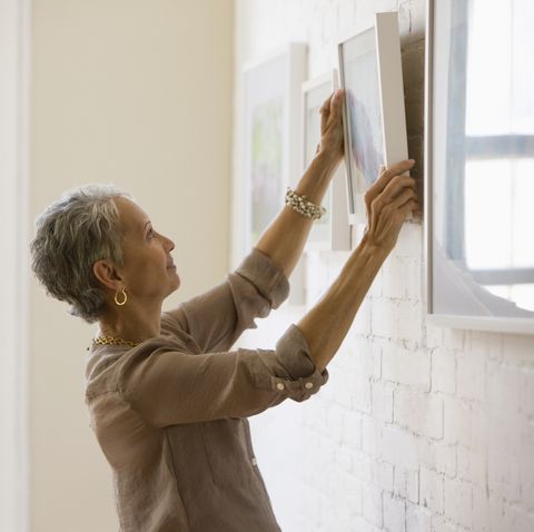 mixed race woman hanging pictures on wall