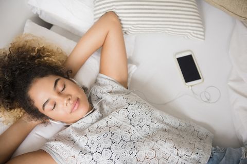mixed race woman laying on bed listening to music on cell phone