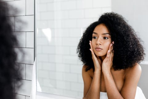 Mixed race woman massaging her face and looking at a mirror