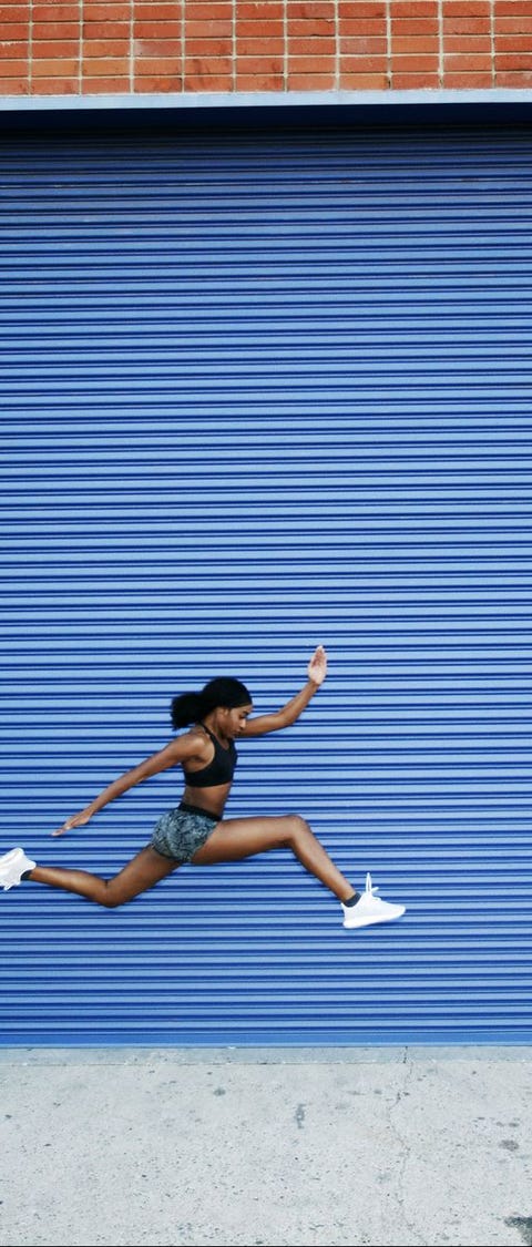 Mixed Race woman running and jumping near blue garage door Mixed Race woman running and jumping near blue garage door