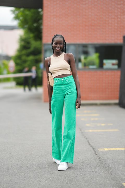 a model wearing a beige cropped tank top, green jeans, and white chunky nike sneakers on the street